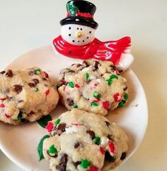 four cookies on a white plate with a snowman figurine in the background