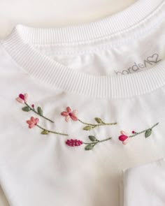 a white shirt with pink flowers embroidered on the front and back, sitting on a table