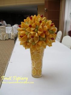 a vase filled with yellow flowers sitting on top of a white table covered in chairs