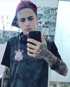 a man with tattoos on his arm holding a cell phone and looking at the camera