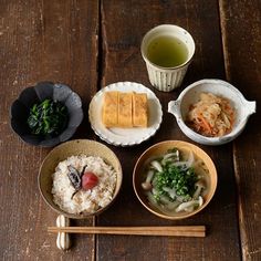 bowls of food and chopsticks sit on a wooden table next to two cups