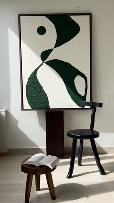 an open book sitting on top of a wooden stool in front of a large painting