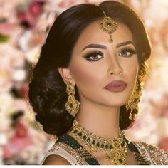 a woman with dark hair and gold jewelry on her head, in front of flowers