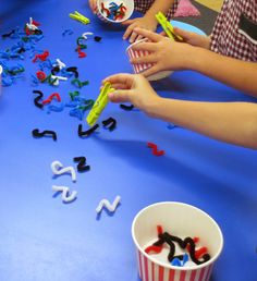 children are sitting at a table with letters and numbers on the blue floor, while one child is holding a plastic cup