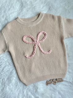 a knitted sweater with a pink bow on the front and back, sitting on a white furnishing