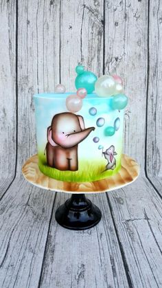 a cake decorated with an elephant and bubbles on a wooden table next to a wall