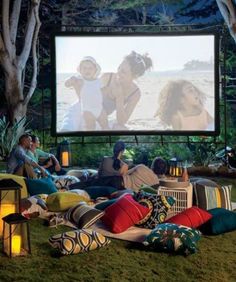 people sitting on the grass watching a movie in front of a large screen with candles