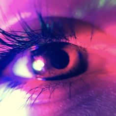 an extreme close up shot of the iris of a person's eye with bright colored lighting