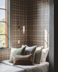 a bed sitting in front of a window with pillows on it's headboard