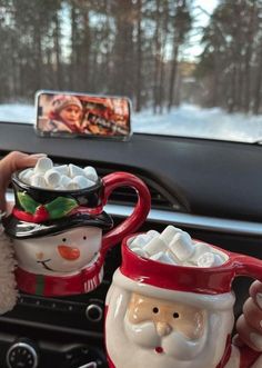 two mugs with santa claus and snowmen on them in front of a car