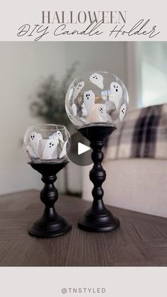 two black candlesticks with ghost decorations on them sitting on a table in front of a couch