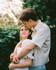 a man and woman embracing each other in front of trees