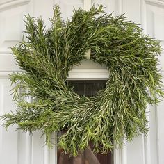 a wreath hanging on the front door of a house with white paint and green foliage