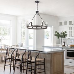 a kitchen with an island and chairs in the middle of it, surrounded by white cabinets