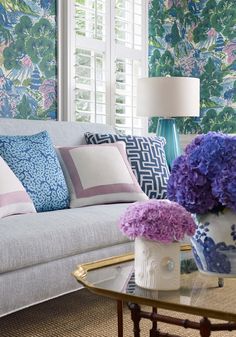 a living room filled with furniture and flowers on top of a coffee table in front of a window