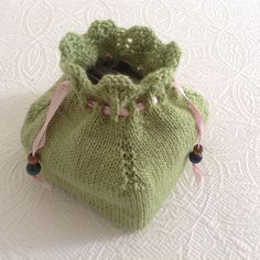 a green knitted bag with pink ribbon around the bottom and handles, sitting on a white surface