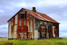 an old rusted building in the middle of a field with tall grass and weeds