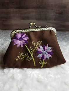 a brown purse with purple flowers embroidered on the front and sides, sitting on a white furnishing