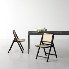 two chairs and a table with some fruit on it in front of a white wall