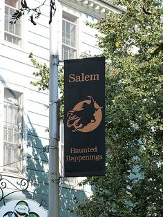 a black and gold sign hanging from the side of a building next to a tree