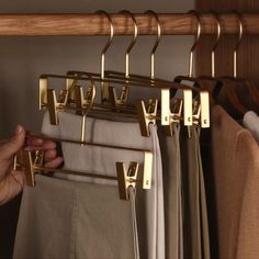 a person is trying to hang clothes on a rail in the closet with gold handles