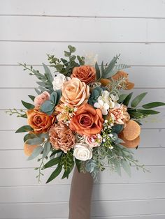 a bridal bouquet with orange, white and pink flowers in front of a wooden wall