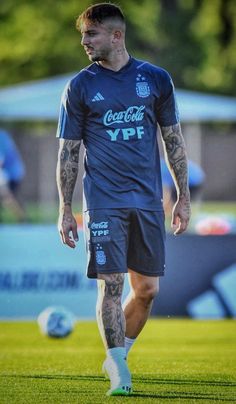 a man with tattoos on his arm and leg walking in the grass near soccer balls