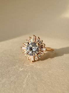 Channel the goddess of marriage with the Hera the Queen engagement ring. Its intricate sunburst design and sparkling lab diamonds create a truly regal and timeless piece. Ring Details 6.5 mm Round Lab Diamond Side Gem: 3.50 MM Faceted, SI2-SI3 Triangle Faceted GHI Genuine Diamond, qty 2 Accent Gems: 3.00 X 01.75 MM Step, SI2-SI3 Tapered Baguette Step GHI Genuine Diamond, 2.50 X 1.50 MM Step, SI2-SI3, Tapered Baguette Step GHI Genuine Diamond 1.70 MM (1.56 - 1.80) Full Cut, SI2-SI3 Round Full Cut G-H Genuine Diamond Average Width: 1.8mm Style: Accented Solitaire Your ring is made-to-order. Our current turnaround time is approximately 3-4 weeks. Your Order Includes: Vintage Style Velvet Ring Box Ethical Sourcing Recycled Precious MetalsMade in USA 123995:609:P Timeless 14k Gold Cluster Ring With Halo, Heirloom 14k Gold Halo Cluster Ring, Heirloom Halo Cluster Ring In 14k Gold, Heirloom 14k Gold Cluster Ring With Halo, Baguette Cut Halo Ring For Anniversary, Wedding Diamond Ring With Cluster Accent Stones, Wedding Cluster Diamond Ring With Accent Stones, Timeless Halo Cluster Ring For Anniversary, 14k Gold Cluster Wedding Ring With Center Stone