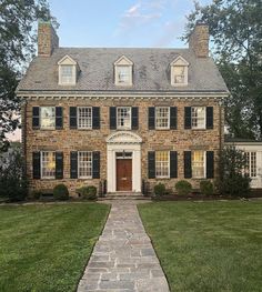 an old brick house with black shutters and stone walkway leading to the front door