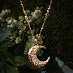 a close up of a necklace with a moon on it and flowers in the background