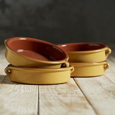 two yellow dishes sitting on top of a wooden table next to each other with one bowl in the middle