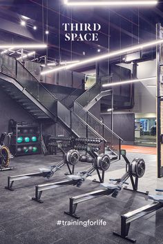 there are many gym equipment in this large room with stairs and lights on the ceiling