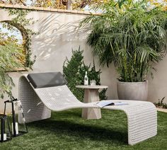 an outdoor lounge chair in the grass next to a potted plant and table with a laptop on it