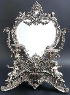 an ornate silver mirror with cherubs on the sides and a heart shaped frame