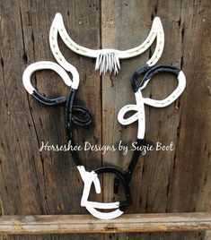 two white and black cow horns are attached to a wooden fence, with the words horse shoe designs by suge boat