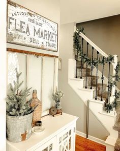 a christmas tree is in a bucket next to a white cabinet and stairs with an old sign on the wall