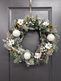 a christmas wreath hanging on the front door with white and gold ornaments, pine cones, silver bells and greenery