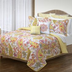 a bed with yellow and pink comforters in a room next to a white curtain