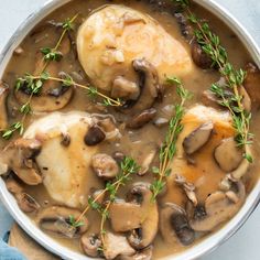 a pan filled with chicken and mushrooms covered in gravy, garnished with fresh herbs