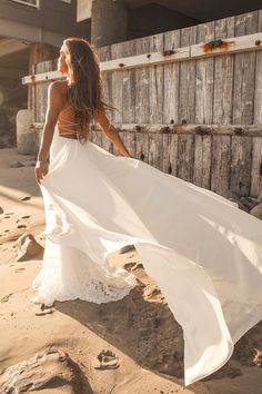 a woman in a white dress is walking on the beach with her long flowing skirt