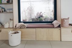 a window seat in front of a large window with plants on the windowsill and bookshelves behind it