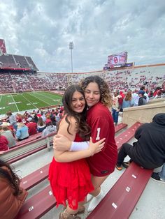 two women hugging each other in front of a stadium full of people and one has her arms around the other