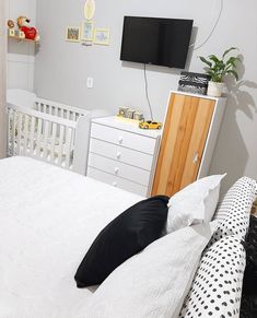 a white bed with black and white pillows in a bedroom next to a tv mounted on the wall