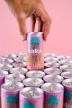 a hand reaching for a can of beer on top of a stack of pink cans