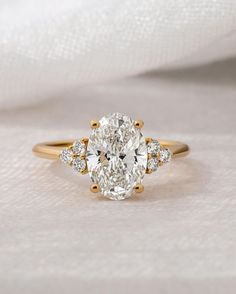 an oval cut diamond ring with three smaller round diamonds on the band, set in 18k yellow gold