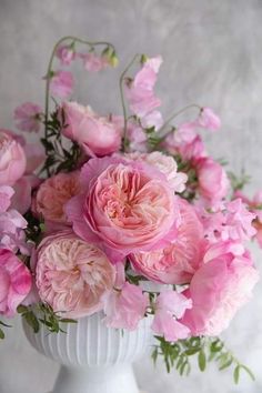 a white vase filled with pink flowers on top of a table