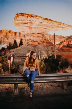 a woman sitting on top of a wooden bench next to a rock formation in the background