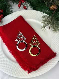 two napkins with rings on them sitting on a plate next to christmas decorations and pine branches