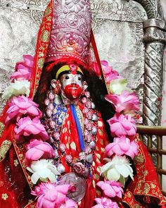 a man dressed in red and gold with flowers around his neck, sitting on a chair