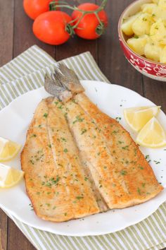 two fish fillets on a white plate with lemons and tomatoes